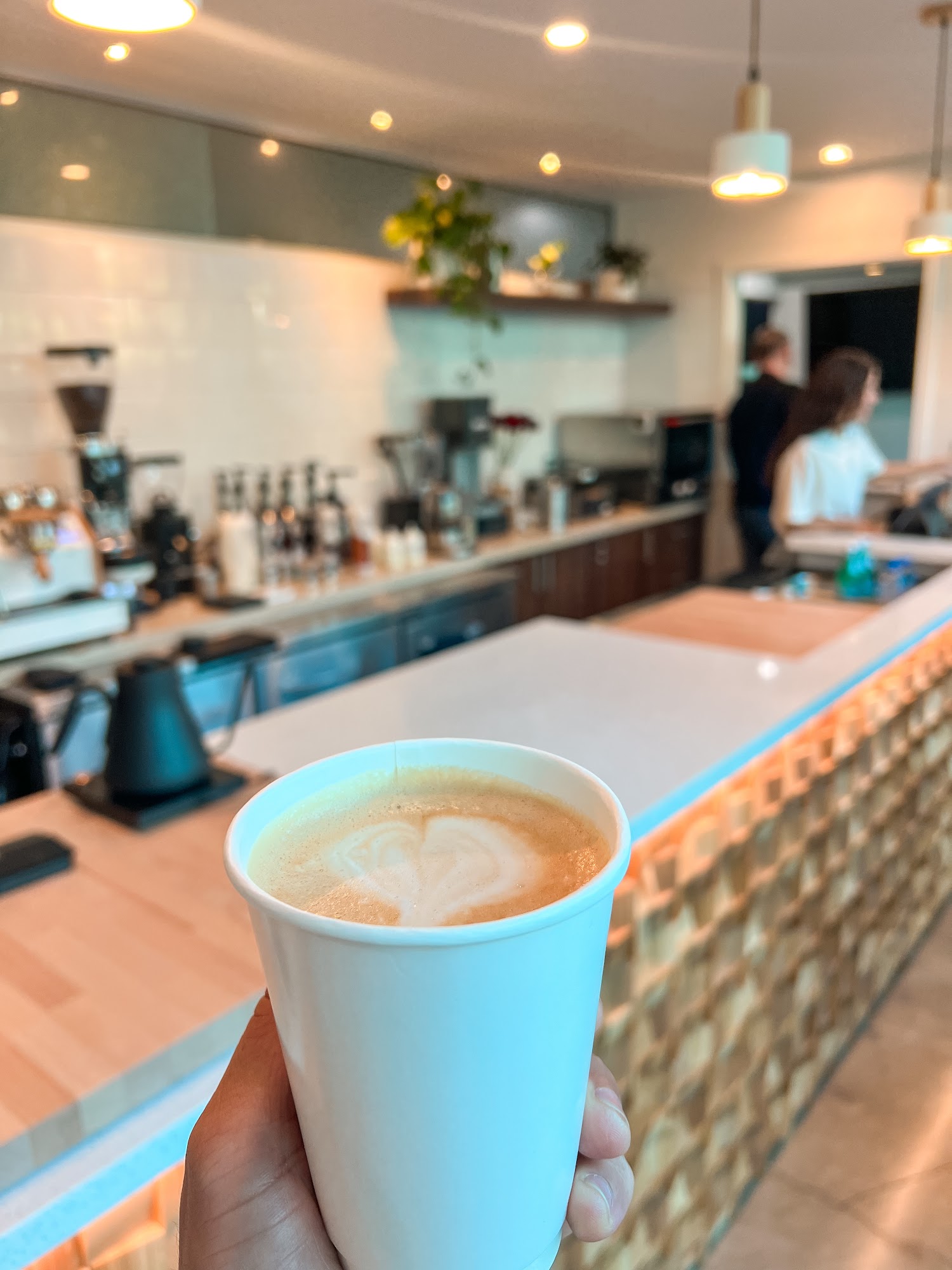 Latte in a white cup held in front of the softly lit Chapola Cafe counter